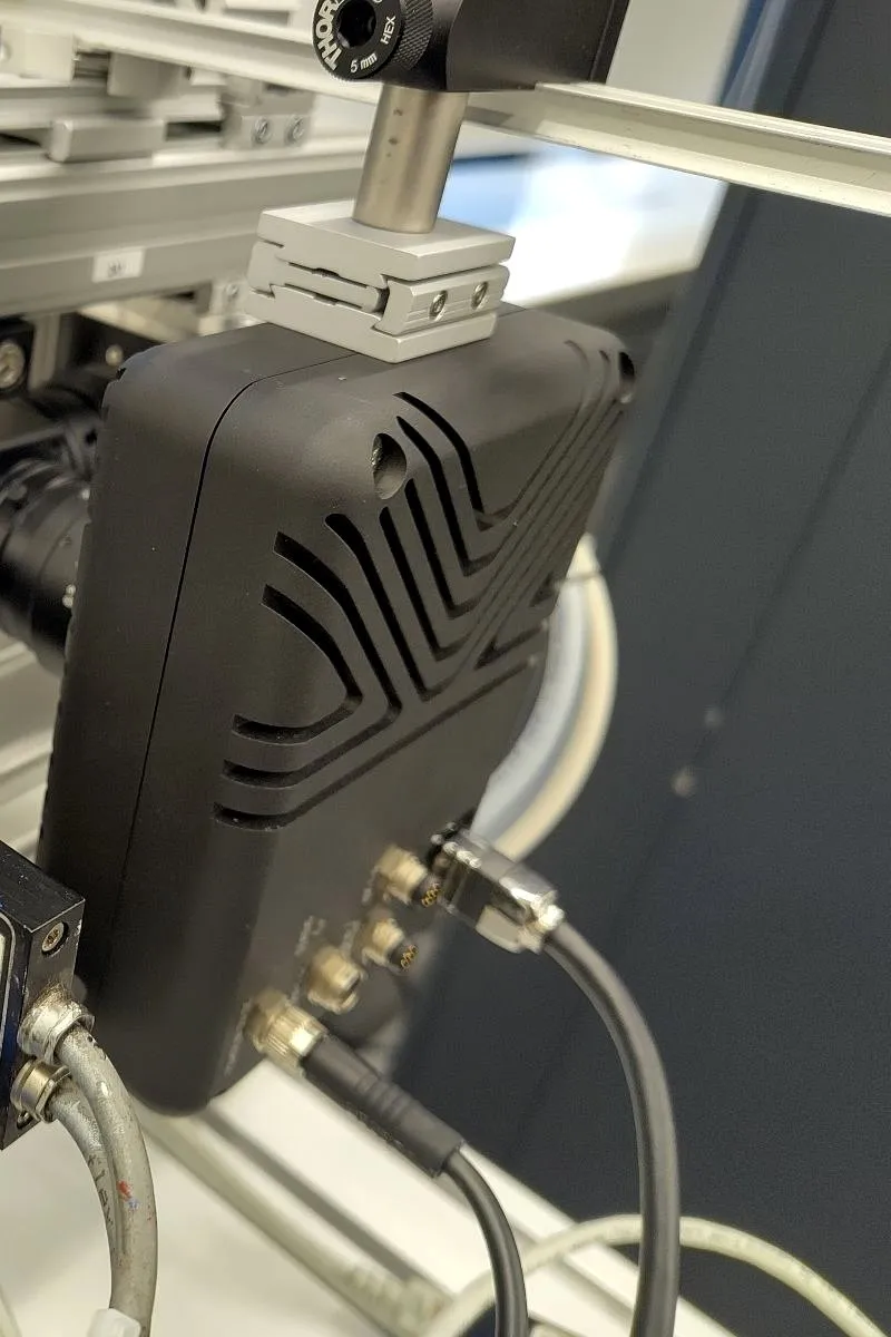 A compact HSCAM camera, sharing the same ridged housing pattern as the STREAMER family, mounted on the motion-stage rig.