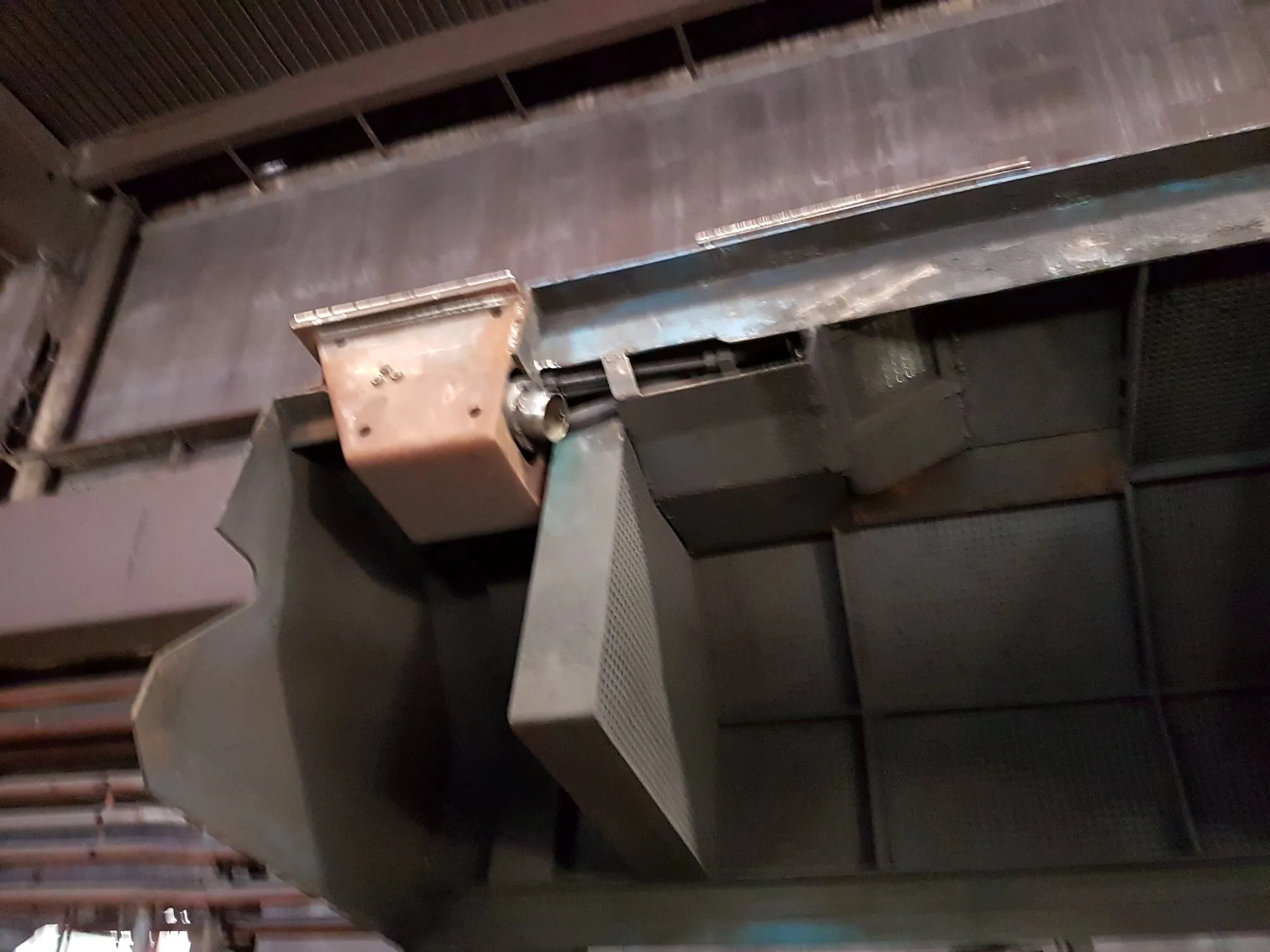 A metal housing mounted on the underside of overhead machinery.