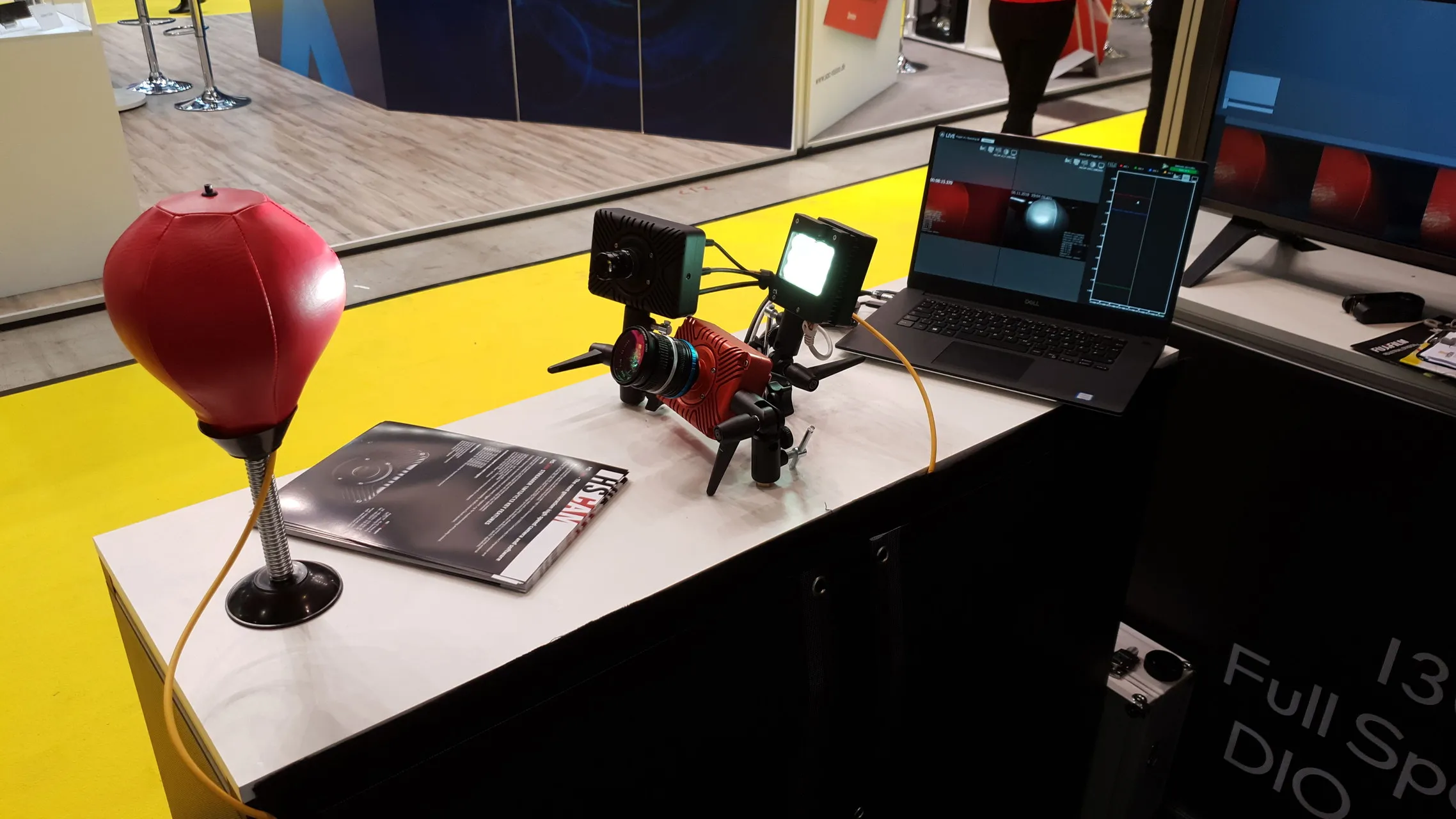 HSCAM demonstration booth at a machine-vision trade fair: two cameras on tripods aimed at a red punching ball, with a laptop showing live dual-camera HSCam Viewer software.